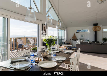 Cut flowers on dining table with plates and view through open doors to decked terrace Stock Photo