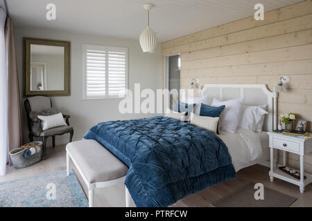 Blue quilt on double bed with wood cladding in coastal home Stock Photo