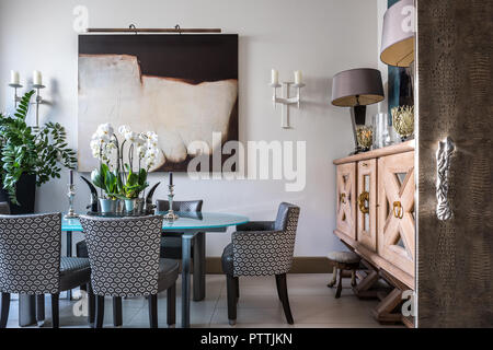 Large wooden sideboard and modern art in dining room with upholstered chairs Stock Photo