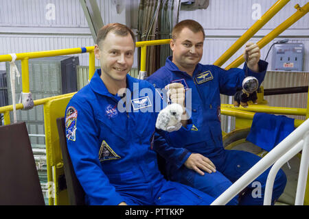 Expedition 57 crew member cosmonaut Alexey Ovchinin of Roscosmos, right, and Nick Hague of NASA hold up toy mascots in their blue jump suits at the Baikonur Cosmodrome October 6, 2018 in Baikonur, Kazakhstan. The two are scheduled to launch on October 11th and will spend the next six months living and working aboard the International Space Station. The mascots will be mounted over their heads in the Soyuz MS-10 spacecraft to serve as “zero-G” indicators when they launch. Stock Photo