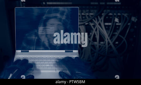 Hacker with laptop on a dark background of structured cabling. Close-up of male hands in black gloves on keyboard, motion blur. Spy's head in hood. Stock Photo