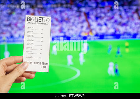 A woman's hand holds a bookmaker's ticket against the backdrop of a game of football, sports betting, the bookmaker's office. BIGLIETTO ufficio di bookmaker-Ticket bookmakers office, tasso-bet, fattore-ratio, viccite complessive-total win Stock Photo