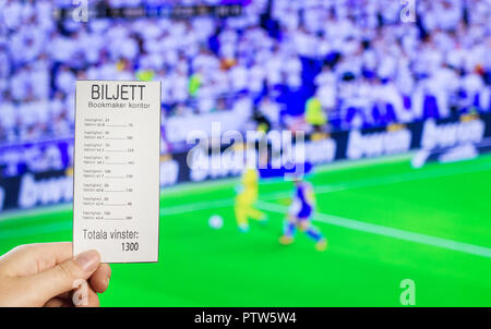 A woman's hand holds a bookmaker's ticket against the backdrop of a game of football, sports betting, the bookmaker's office. Biljett Bookmaker kontor-Ticket bookmakers office, hastighet-bet, faktor-ratio, totala vinster -total win Stock Photo