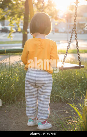 Turned back little baby girl with bob haircuts, chain children swing in the park outdoor Stock Photo