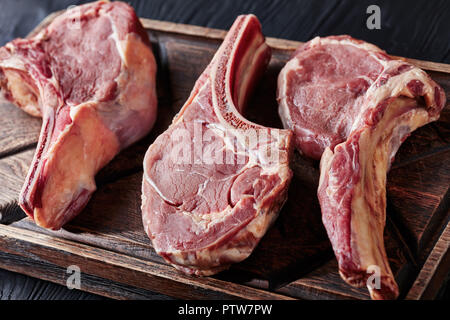 three Dry aged raw tomahawk beef steaks on an old rude wooden cutting board, close-up Stock Photo