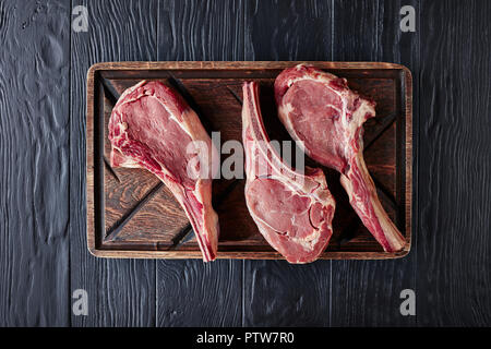three Dry aged raw tomahawk beef steaks on an old rude wooden cutting board, close-up, flat lay, view from above Stock Photo