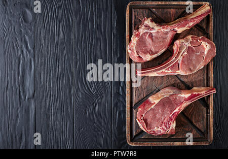 three Dry aged raw tomahawk beef steaks on an old rude wooden cutting board, close-up, flat lay, view from above, copy space Stock Photo