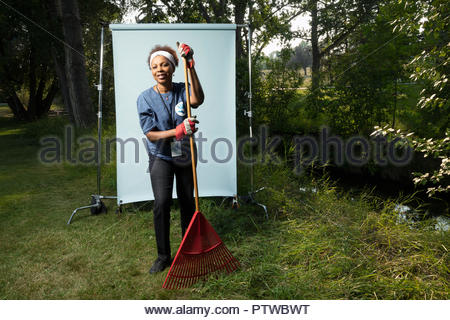 Portrait smiling senior female volunteer with rake against white background in park