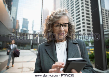 Senior businesswoman using smart phone on city sidewalk
