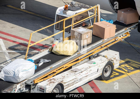 Aircraft ramp loader loading baggage to conveyor belt on airport apron ...