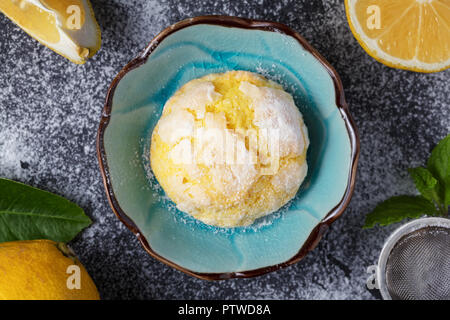 Single Homemade  lemon crinkle cookie with powdered sugar icing. Cracked citrus biscuit on small blue plate and dark background Stock Photo