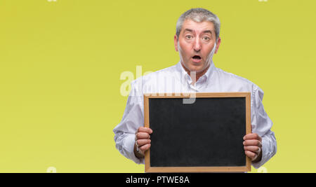 Handsome senior teacher man holding blackboard over isolated background scared in shock with a surprise face, afraid and excited with fear expression Stock Photo