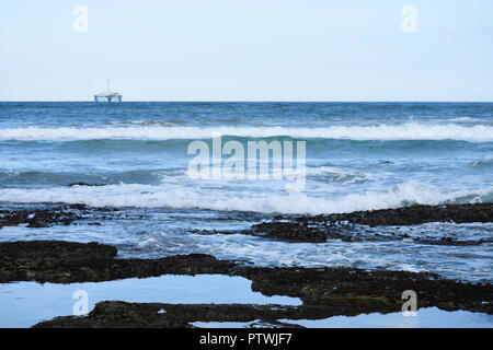 Rock Pools On Sea Shore With Ocean Horizon And Oil Drilling Platform In The Distance Stock Photo