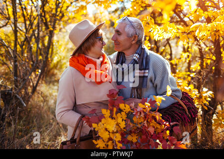 Senior couple walking in autumn forest. Middle-aged man and woman hugging and chilling outdoors. People holding basket for picnic Stock Photo