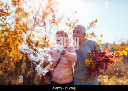 Senior couple walking in autumn forest. Middle-aged man and woman blowing fluffy seeds. People having fun outdoors Stock Photo