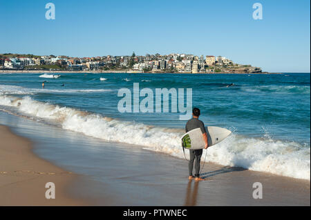 21.09.2018, Sydney, New South Wales, Australia - A surfer is seen holding his surfboard as he gazes at the open ocean at Bondi Beach. Stock Photo