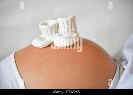 Woman in ninth month pregnant,, baby shoes on belly, Germany Stock Photo
