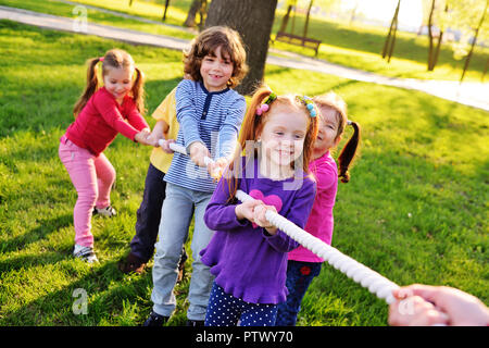 a group of small preschool children play a tug of war in the park. Outdoor games, childhood, friendship, leadership, children's day. Stock Photo