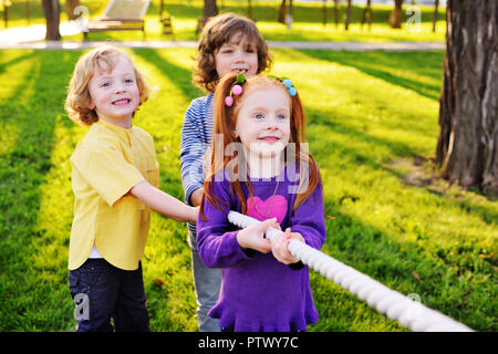 a group of small preschool children play a tug of war in the park. Outdoor games, childhood, friendship, leadership, children's day. Stock Photo