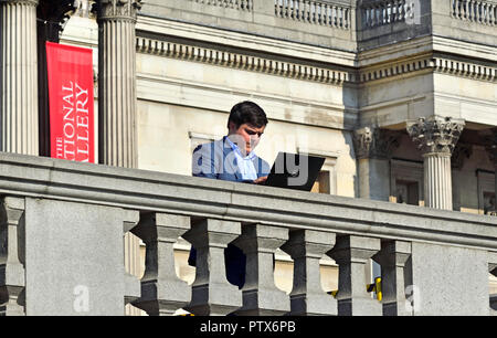 Businessman using his laptop computer in Trafalgar Square, London, England, UK. Stock Photo