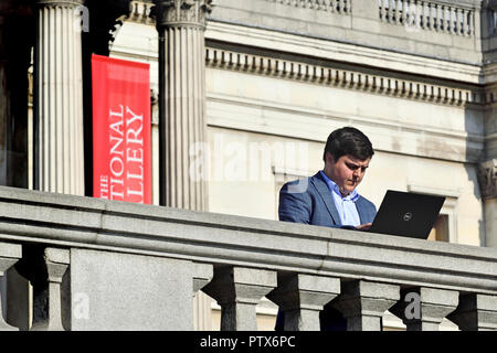 Businessman using his laptop computer in Trafalgar Square, London, England, UK. Stock Photo