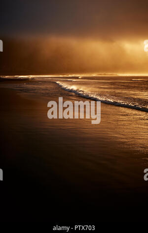 An empty windswept beach in the low morning sunlight on a stormy day with low clouds and rain - minimal weather coast landscape Stock Photo