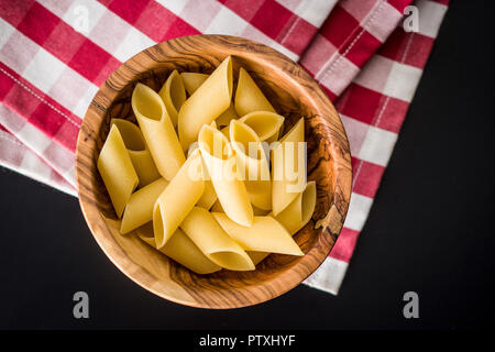 Uncooked penne pasta in bowl on kitchen table. Stock Photo