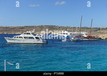 Excursion boats and private yachts moored at Blue Lagoon, Camino Island, with Gozo in the background. The Lagoon is famous for its crystal-clear water. Stock Photo