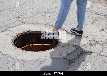 The girl steps into the open sewer hatch Stock Photo