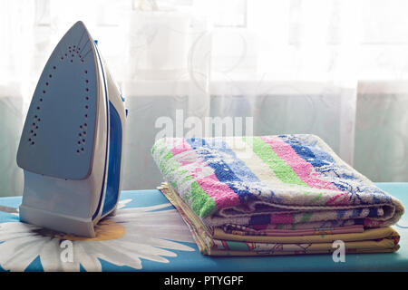 Iron and a stack of towels on the ironing board, close-up Stock Photo