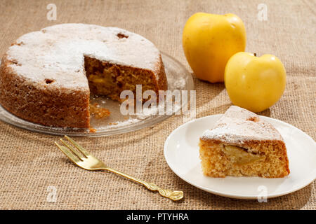 Sliced homemade apple pie on glass plate and piece of pie on white ceramic plate with fork and yellow apples on the background Stock Photo