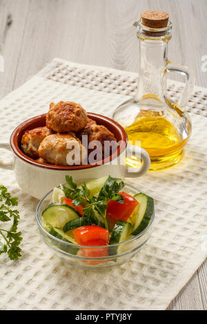 Fried meat cutlets in ceramic soup bowl, bottle with sunflower oil and salad of fresh cucumbers and tomatoes in glass bowl decorated with branch of fr Stock Photo