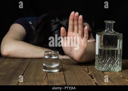 Drunk girl lies on the table, hand shows stop, black background, on table alcohol Stock Photo