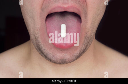 Unshaven man holding a tablet on his tongue, black background, close-up Stock Photo