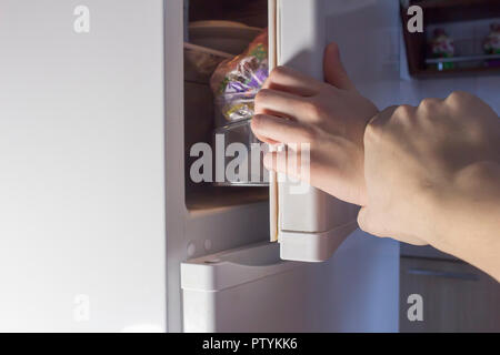 Hand opening fridge at night, diet Stock Photo