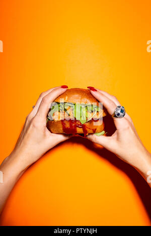 Female hand holding chicken burger against orange background. Stock Photo