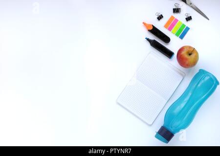 Study stuff. Education background. Stationery. Aspects of education. Stickers, bottle, markers, scissors, clips, apple and notebook on the table. Stock Photo