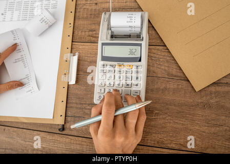 Top view of female accountant using adding machine with documents and receipts on her office desk. Stock Photo