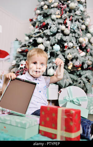 baby boy opens boxes with gifts under the Christmas tree and smiles Stock Photo