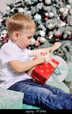 baby boy opens boxes with gifts under the Christmas tree and smiles Stock Photo