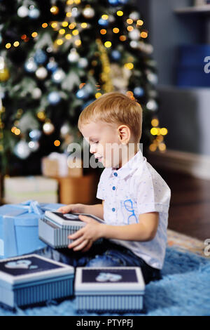 baby boy opens boxes with gifts under the Christmas tree and smiles Stock Photo