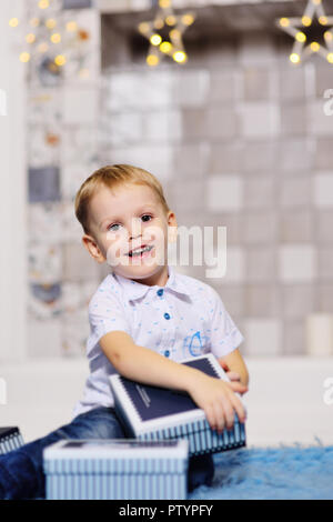 baby boy opens boxes with gifts under the Christmas tree and smiles Stock Photo