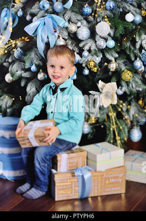 baby boy opens boxes with gifts under the Christmas tree and smiles Stock Photo