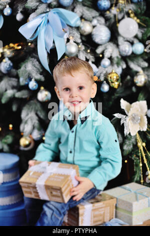 baby boy opens boxes with gifts under the Christmas tree and smiles Stock Photo