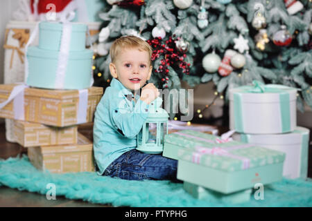 baby boy opens boxes with gifts under the Christmas tree and smiles Stock Photo