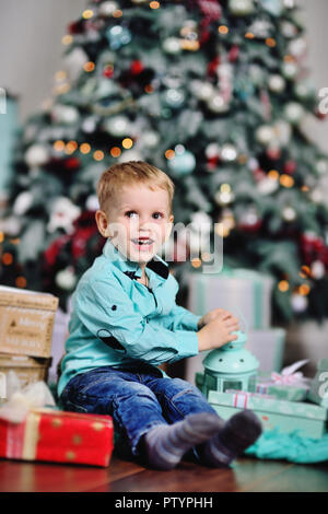 baby boy opens boxes with gifts under the Christmas tree and smiles Stock Photo