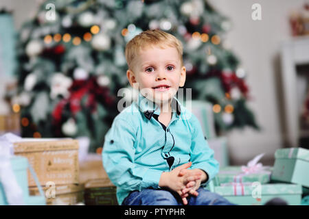baby boy opens boxes with gifts under the Christmas tree and smiles Stock Photo