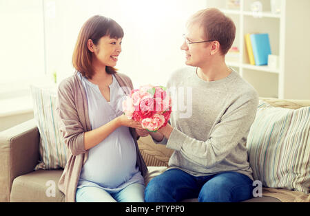 happy husband giving flowers to his pregnant wife Stock Photo