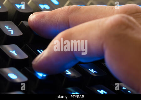 Fingers from the hand of a man typing on a backlit computer keyboard. Stock Photo