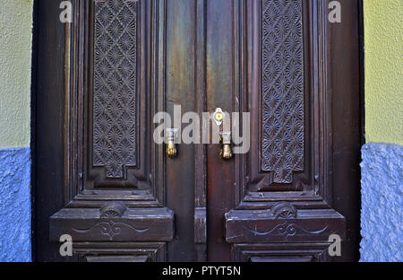 The proud front door of a home in Arganil, Central Portugal, displaying two brass hand door knockers and ornate carved wooden doors. Stock Photo